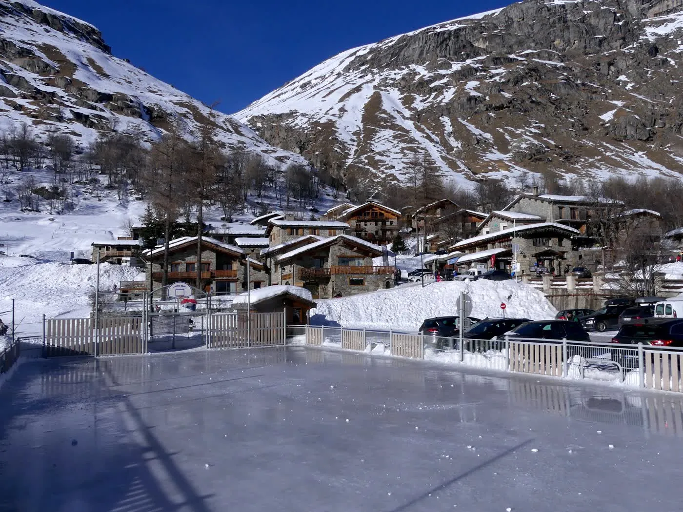 Une patinoire extérieure de village alpin en hiver, sa piste de glace entourée de chalets et de montagnes